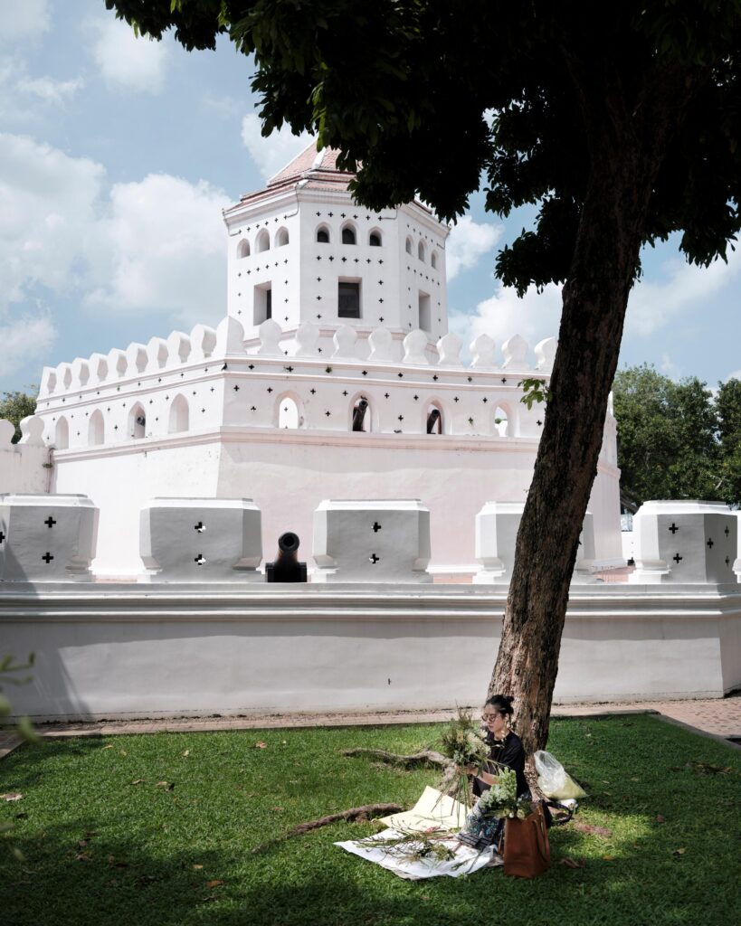 Ayre Wongchaksu arranging flowers on the grass near a white fort in Bangkok.