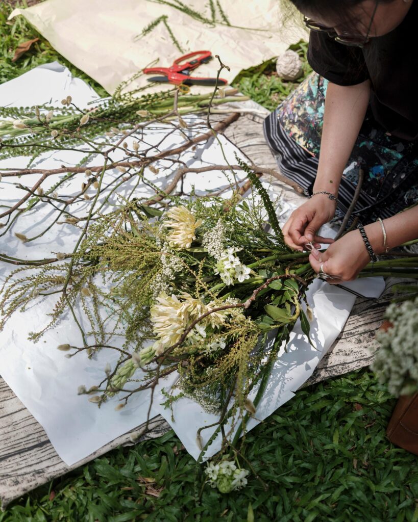 Ayre Wongchaksu's hands arranging flowers and branches on a cloth in a Bangkok park.