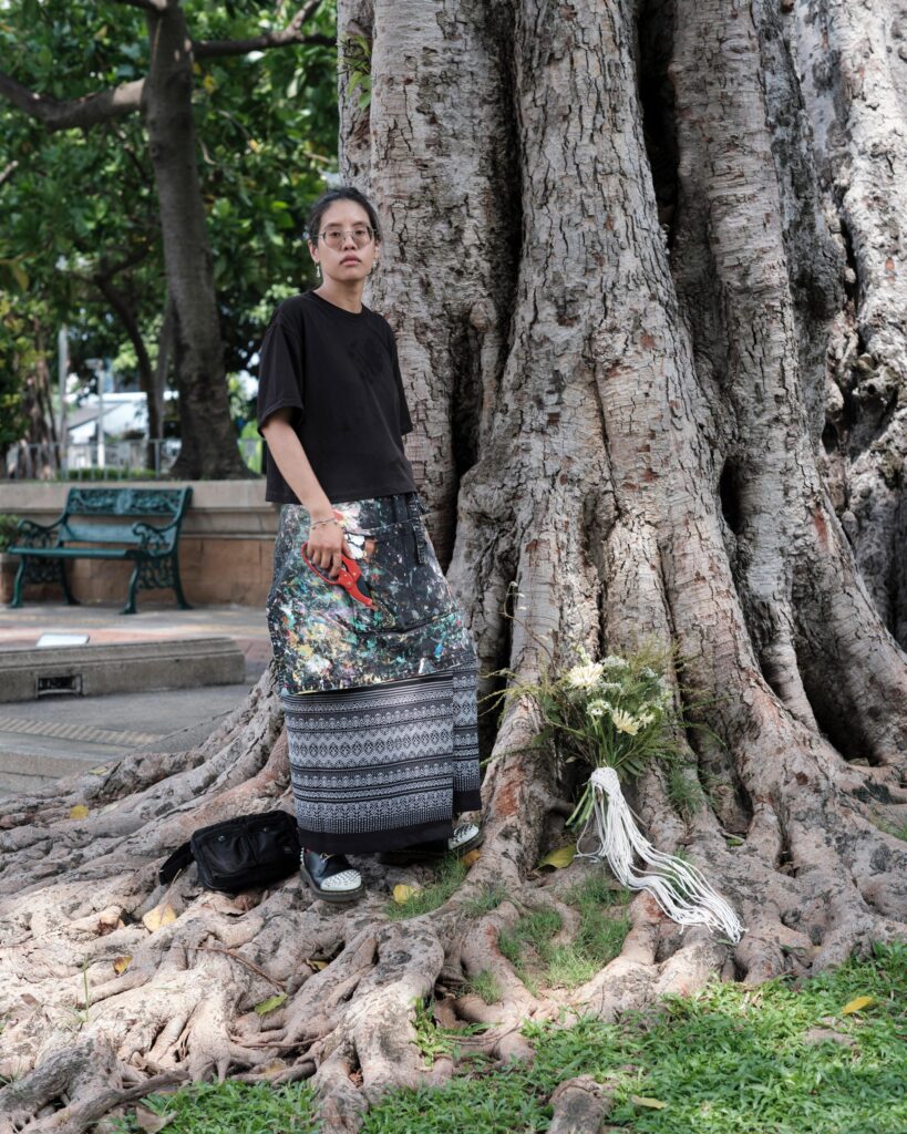 Ayre Wongchaksu holding a bouquet beside the exposed roots of a large tree in Bangkok.