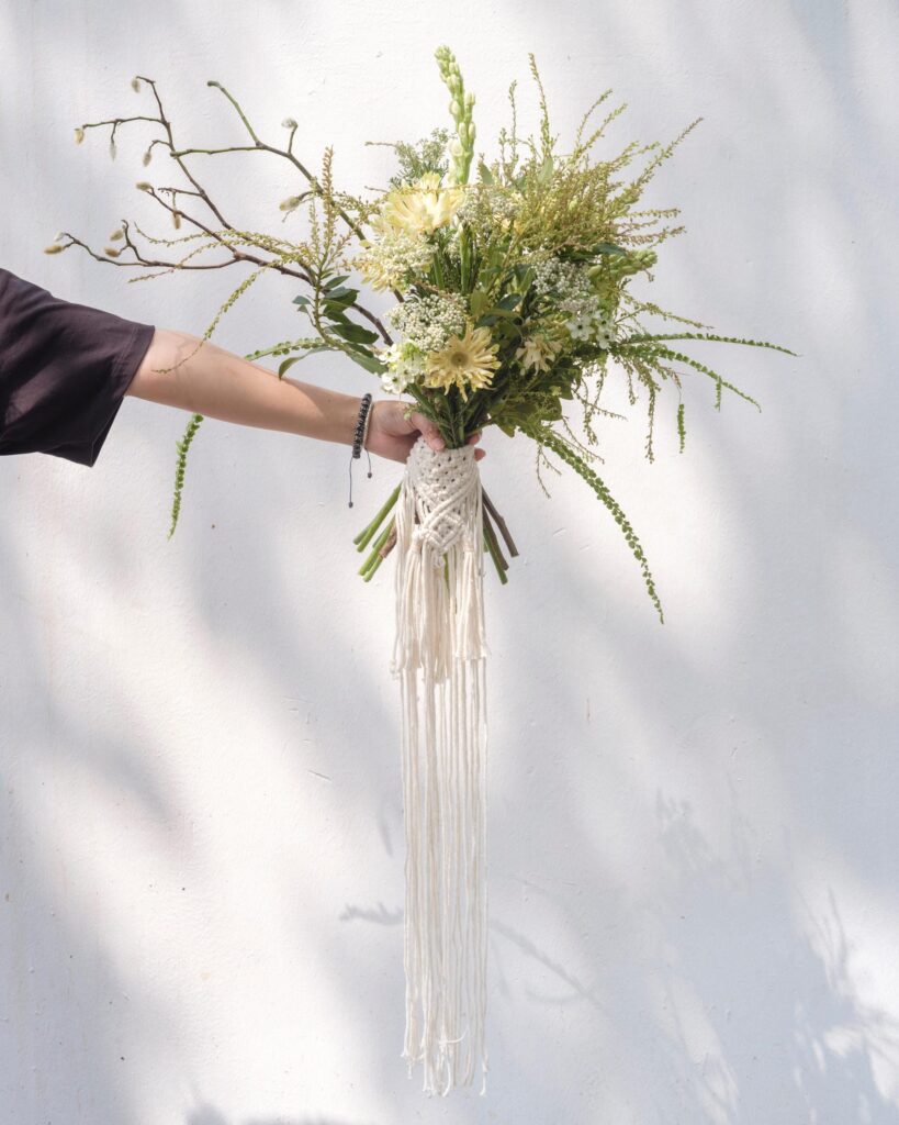 Bouquet of flowers and branches held against a sunlit white wall during Ayre Wongchaksu's Bangkok portrait session.