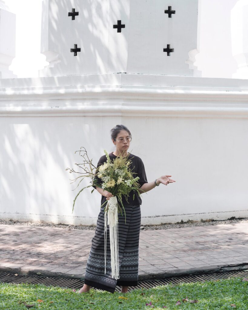 Ayre Wongchaksu holding a sculptural bouquet in front of a white fort wall in Bangkok.