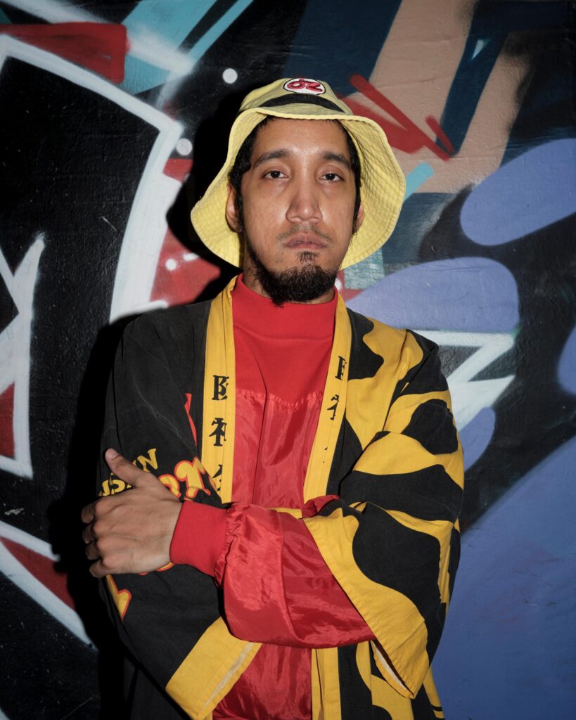 Banana Freeman in a red outfit and yellow-and-black jacket before graffiti in Bangkok.