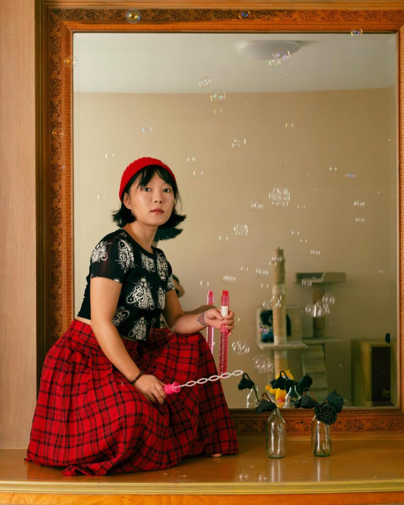 Chun Li holding a bubble wand in front of a mirror at home in Bangkok.