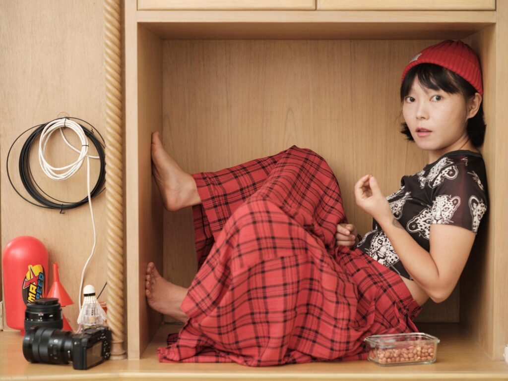 Chun Li curled inside a wooden cabinet at home in Bangkok.