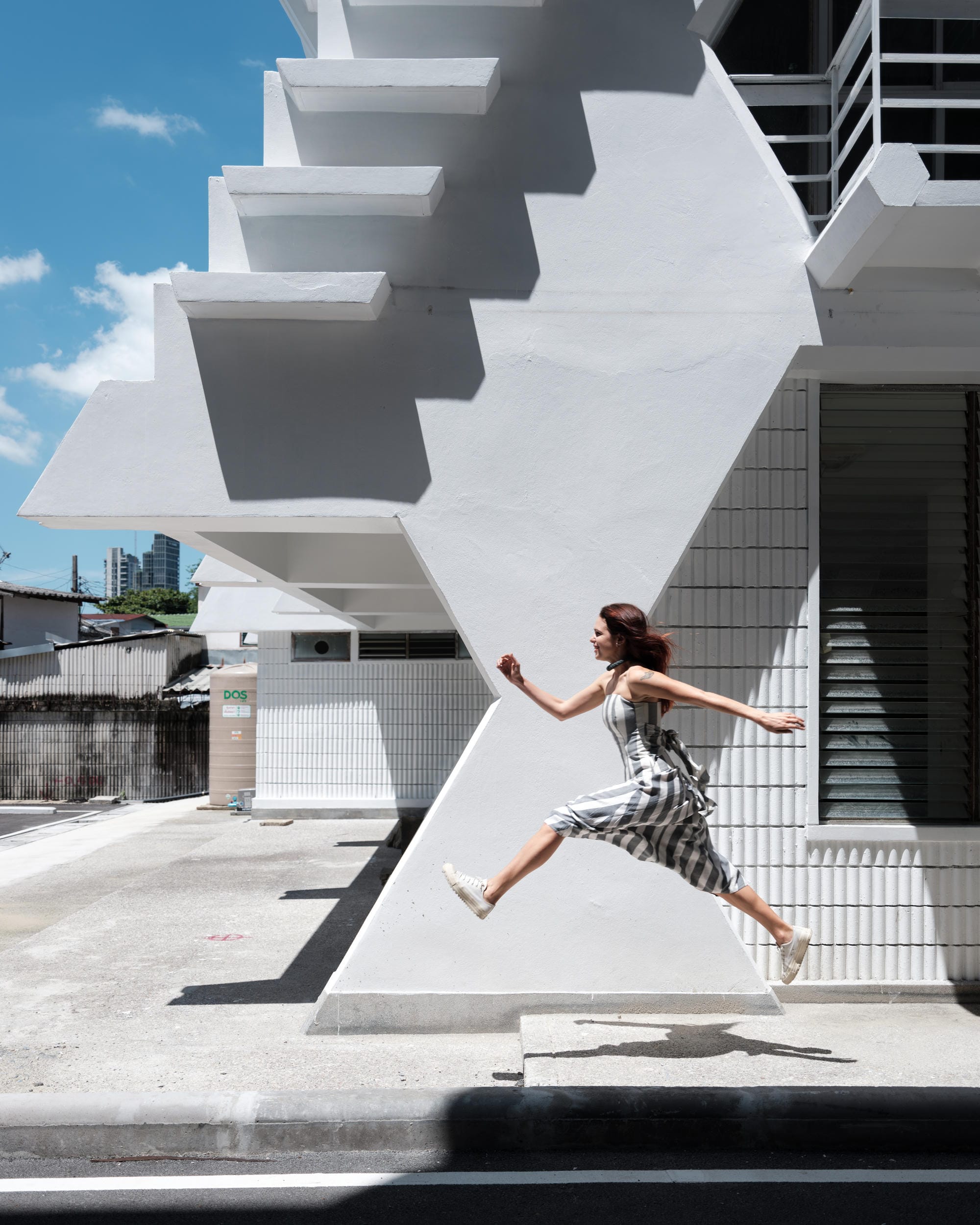 Elena Boni jumping beside an exterior concrete staircase in Bangkok.