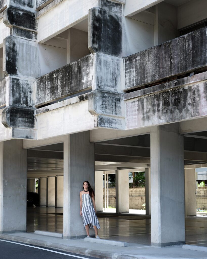 Elena Boni standing beneath a weathered concrete apartment building in Bangkok.