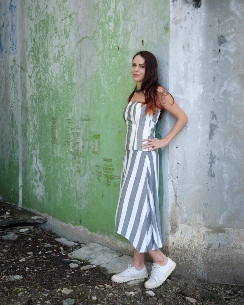 Elena Boni standing against a wall stained with green moss in Bangkok.