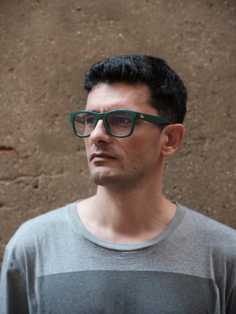 Close portrait of François Cambe wearing green glasses against a textured wall in Bangkok.