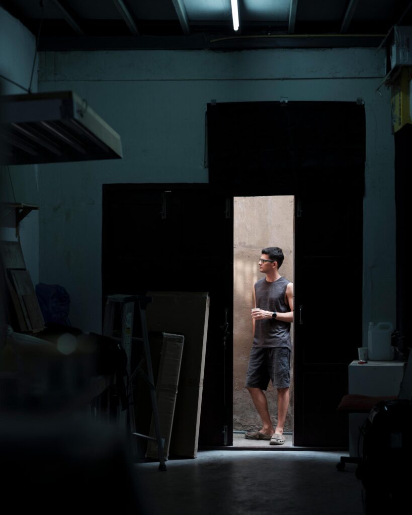 François Cambe standing in a sunlit doorway viewed from his dark Bangkok studio.