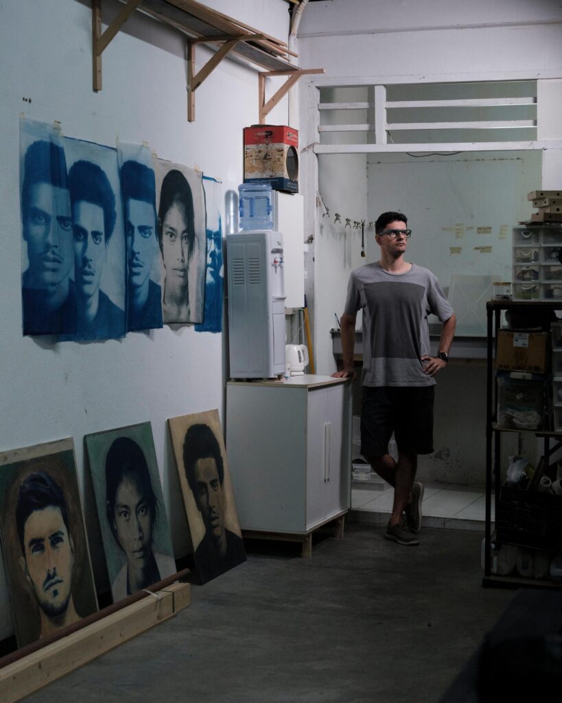 François Cambe walking past portrait prints and paintings in his Bangkok studio.