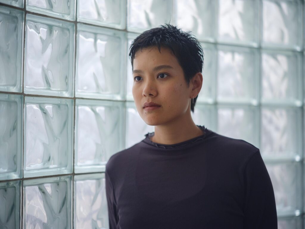 Hutsama Juntaratana standing in front of glass blocks in Bangkok.