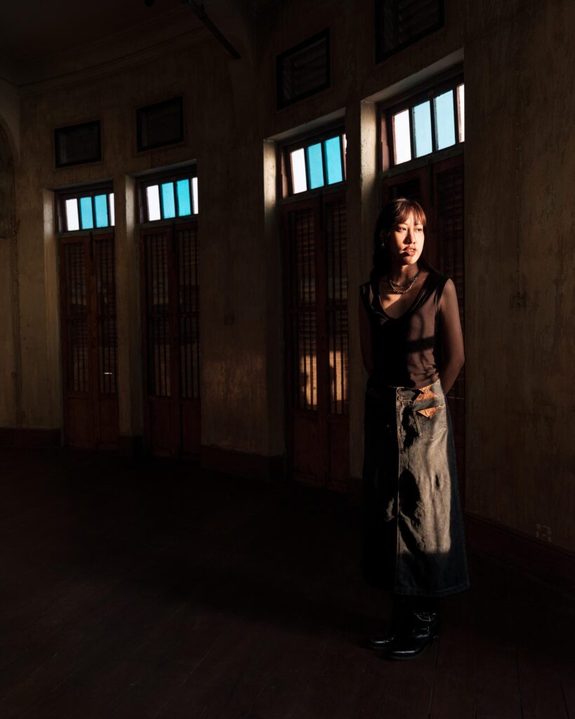 Issiree Shereen Sarntisart standing in a dark wooden room lit by high windows in Bangkok.