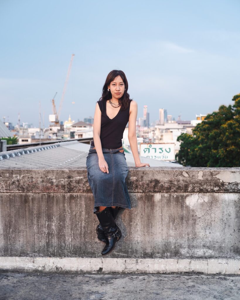 Issiree Shereen Sarntisart sitting on a rooftop ledge above Bangkok.
