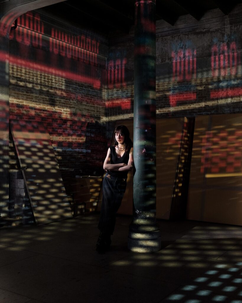 Issiree Shereen Sarntisart standing amid colourful projections in a Bangkok interior.