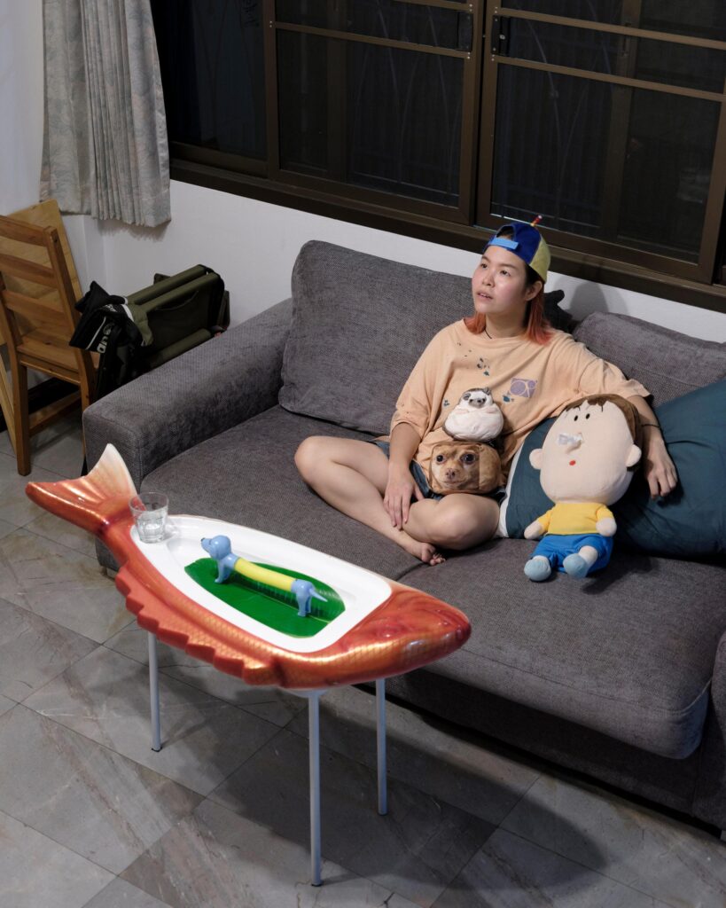 Jib Peerada (StupidShit) sitting on a sofa with a dog and a soft toy in Bangkok.