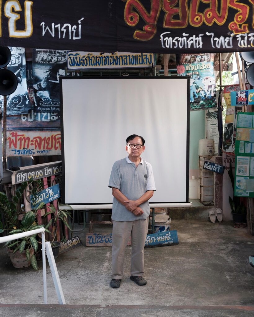 Manit Worachat standing before a projection screen surrounded by movie posters in Lampang.
