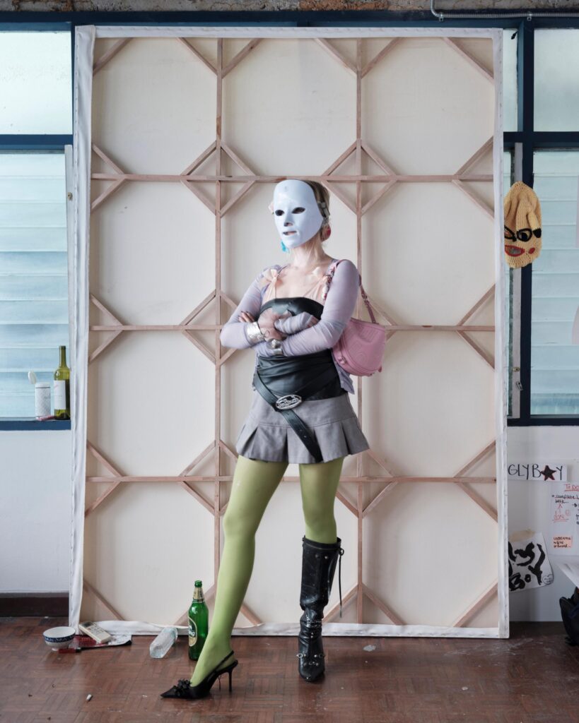 Mascha Serga wearing a white mask in front of a stretched canvas in her Bangkok studio.