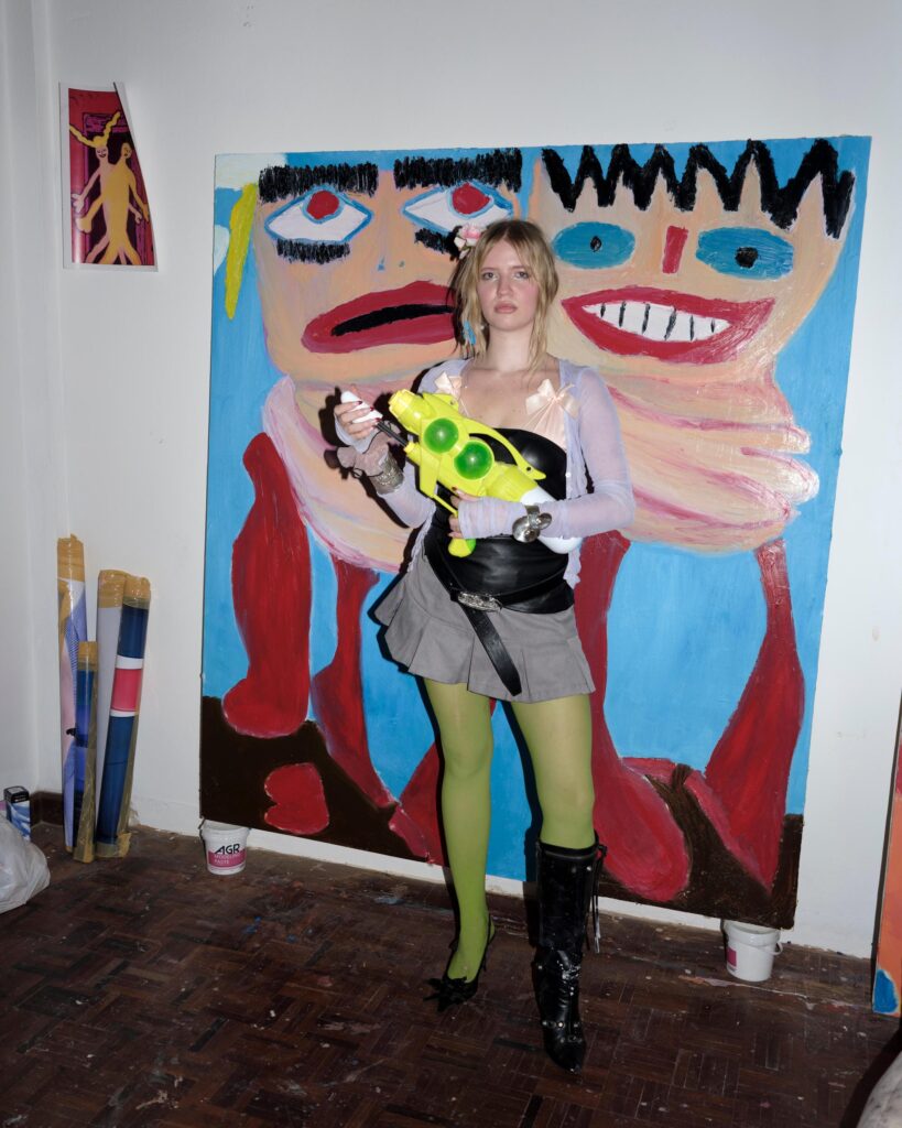 Mascha Serga holding a toy water gun in front of a colourful painting in Bangkok.