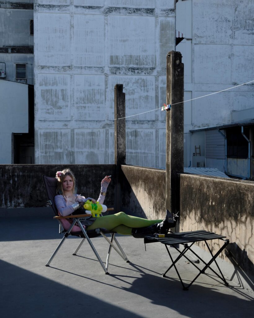 Mascha Serga reclining between folding chairs on a Bangkok rooftop.