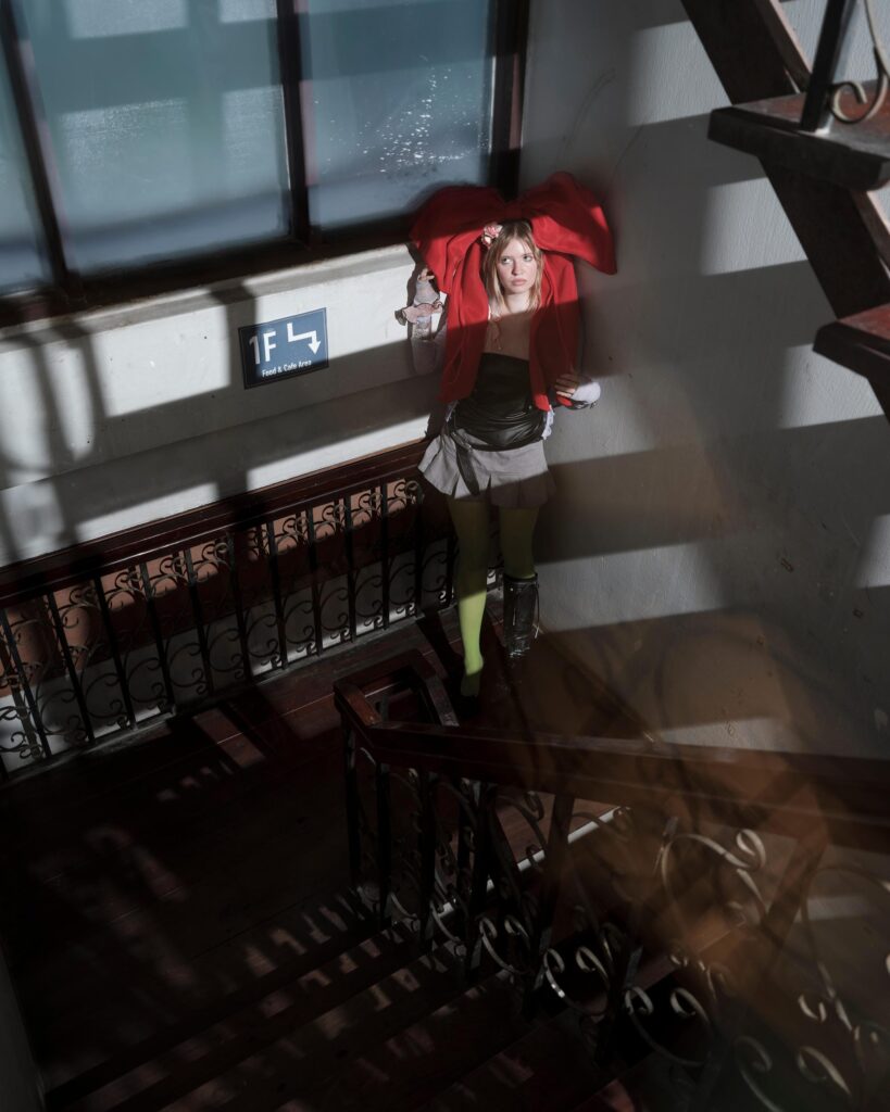 Mascha Serga holding a red shirt against her shoulders in a sunlit Bangkok interior.