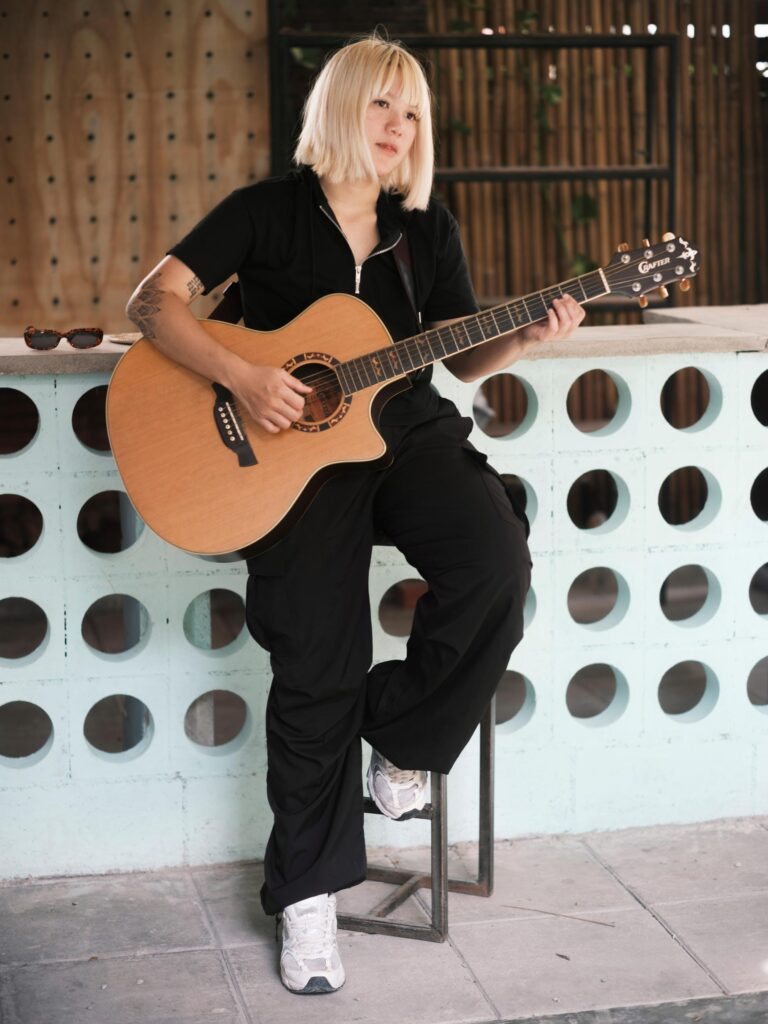 Nadia Mania playing an acoustic guitar while seated on a stool in Chiang Mai.