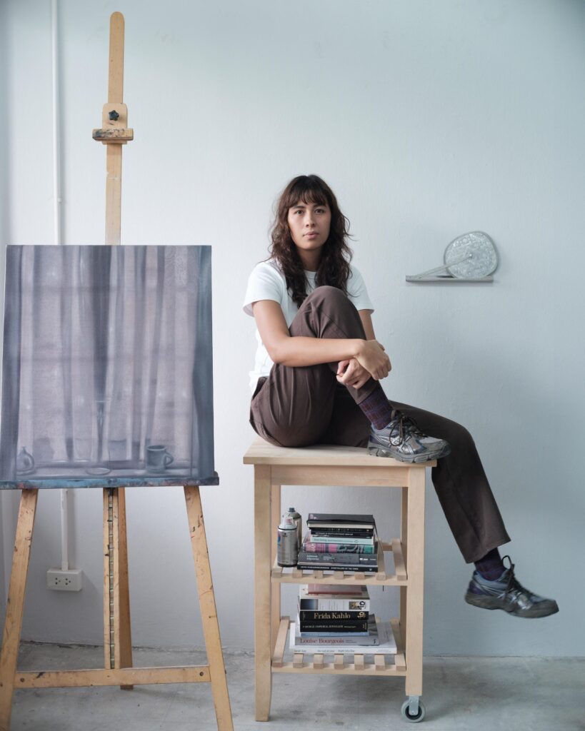 Natalie Sasi Organ seated on a wheeled shelf beside a painting on an easel in Bangkok.