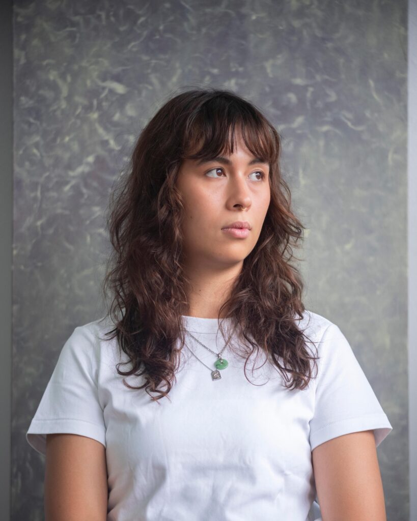 Close portrait of Natalie Sasi Organ in a white shirt against a grey studio wall in Bangkok.