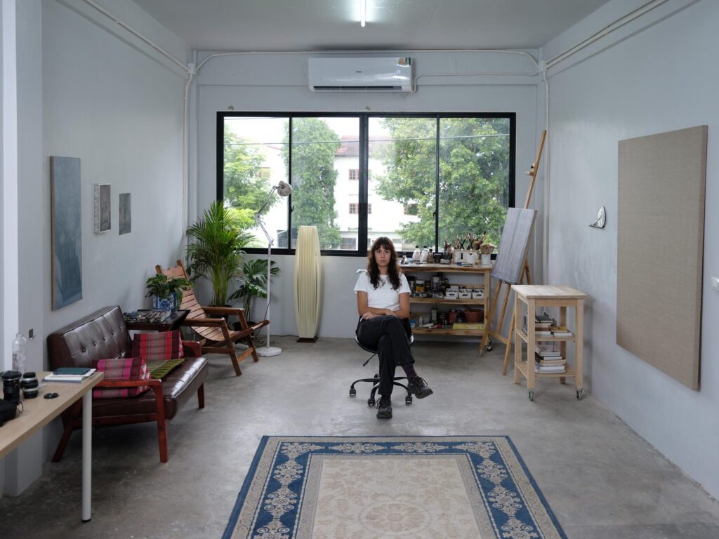 Natalie Sasi Organ seated in the centre of her Bangkok studio, surrounded by plants and artworks.
