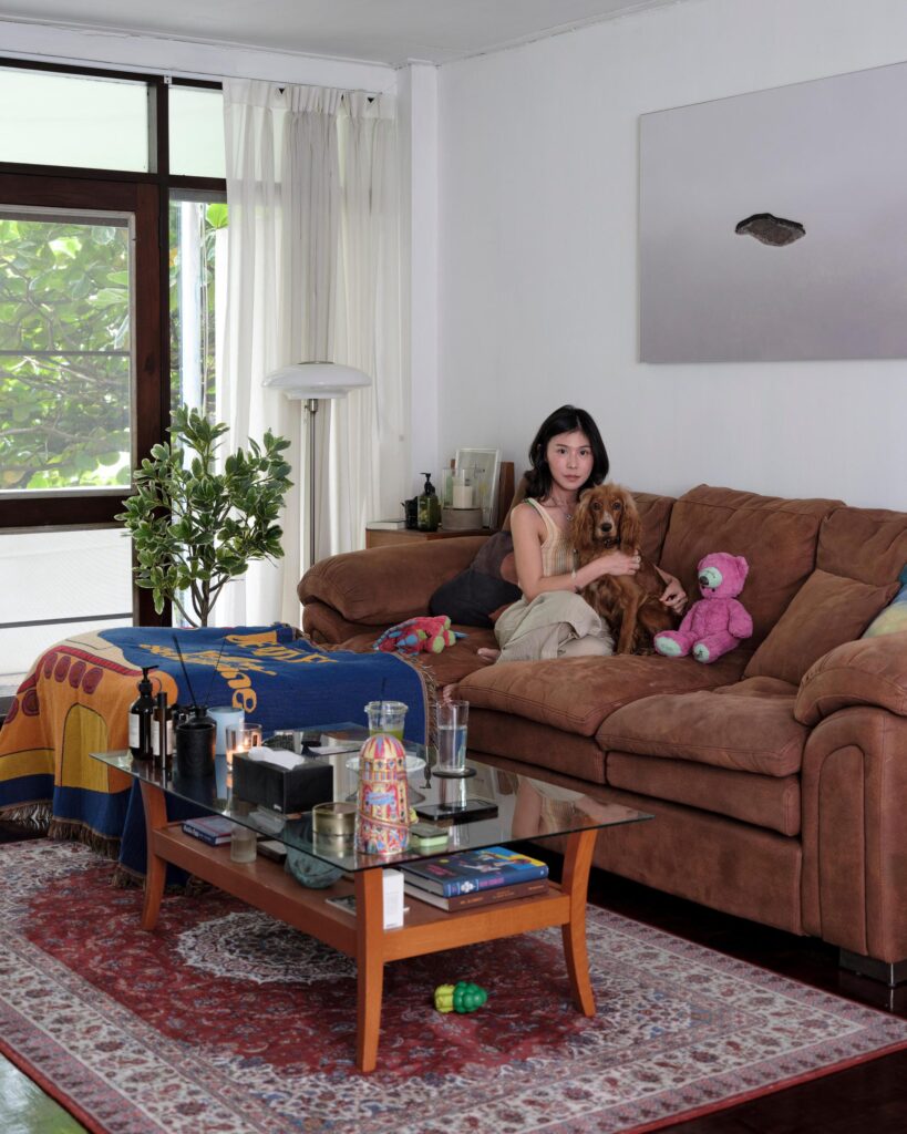Pahparn Sirima seated on a brown sofa beside colourful soft toys in her Bangkok apartment.