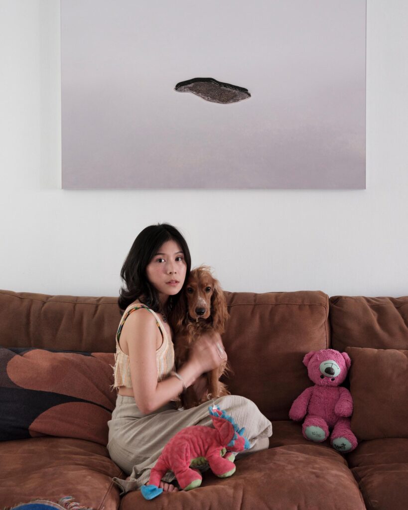 Pahparn Sirima holding a dog on a sofa beneath a photograph in Bangkok.