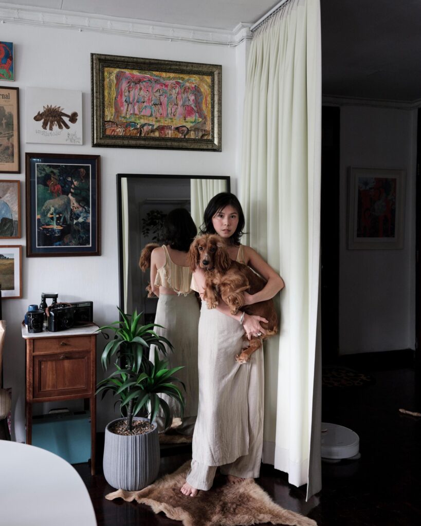 Pahparn Sirima holding a dog among framed artworks in her Bangkok apartment.