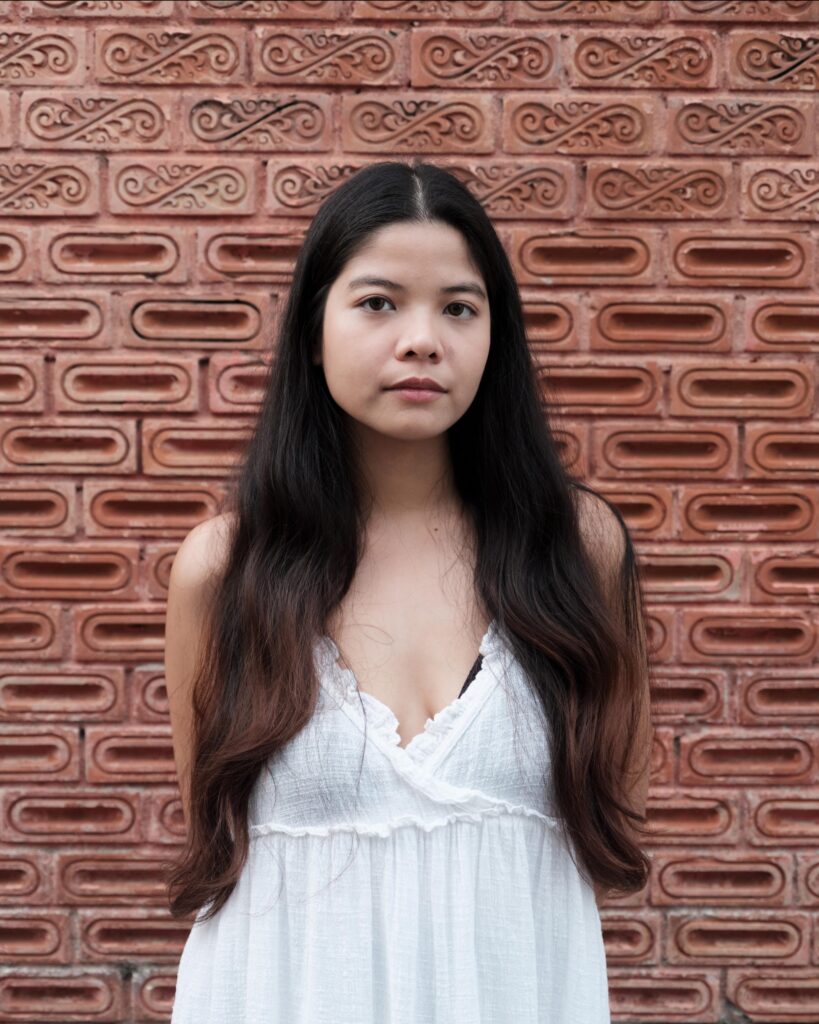 Pavee Vaidyanond standing against a patterned brick wall in Bangkok.