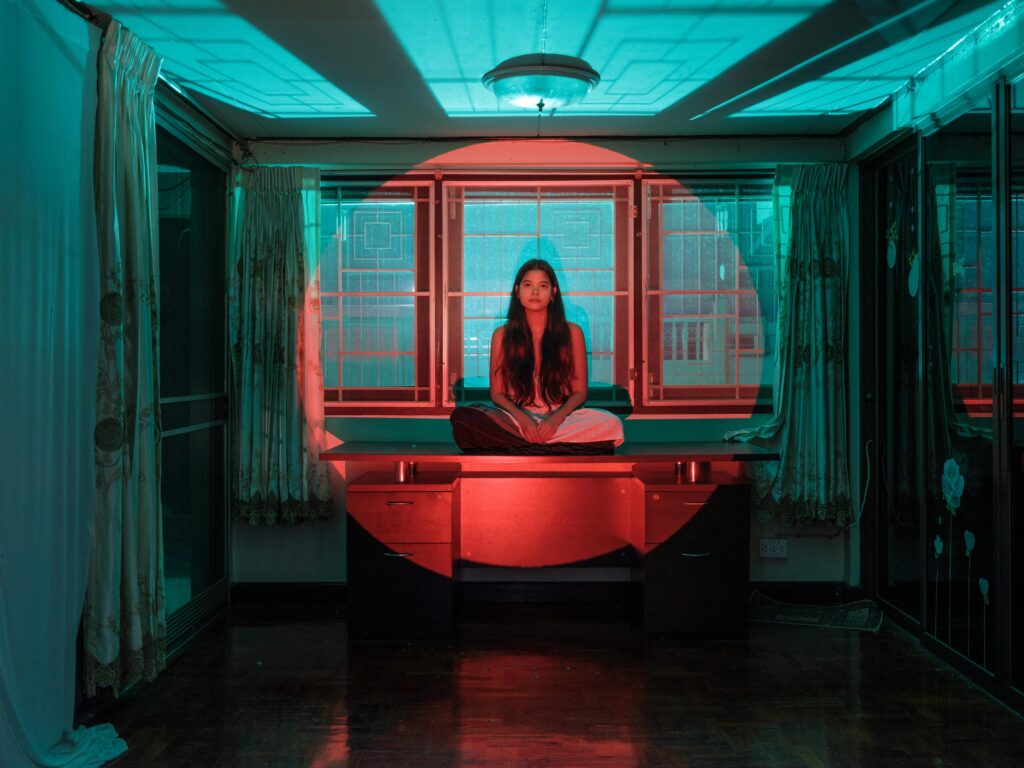Pavee Vaidyanond sitting on a table in a room lit red and turquoise in Bangkok.