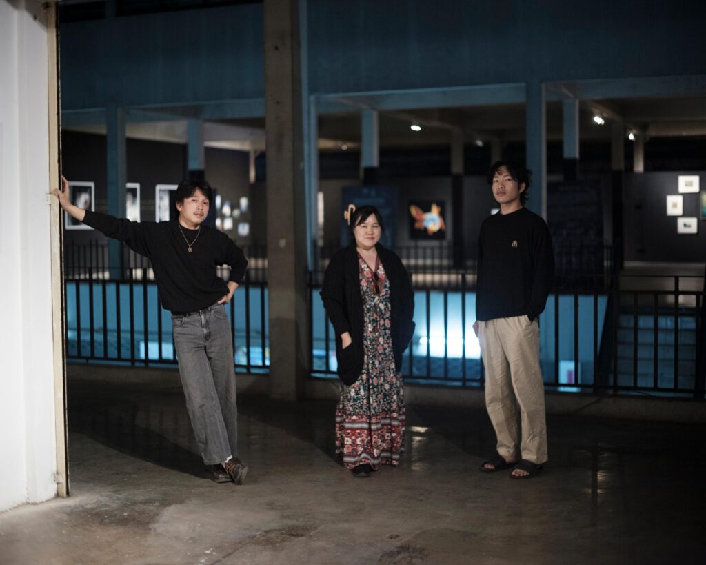 Peerapon Boonthep with two other people beside an exhibition at Artcade Gallery in Phayao.
