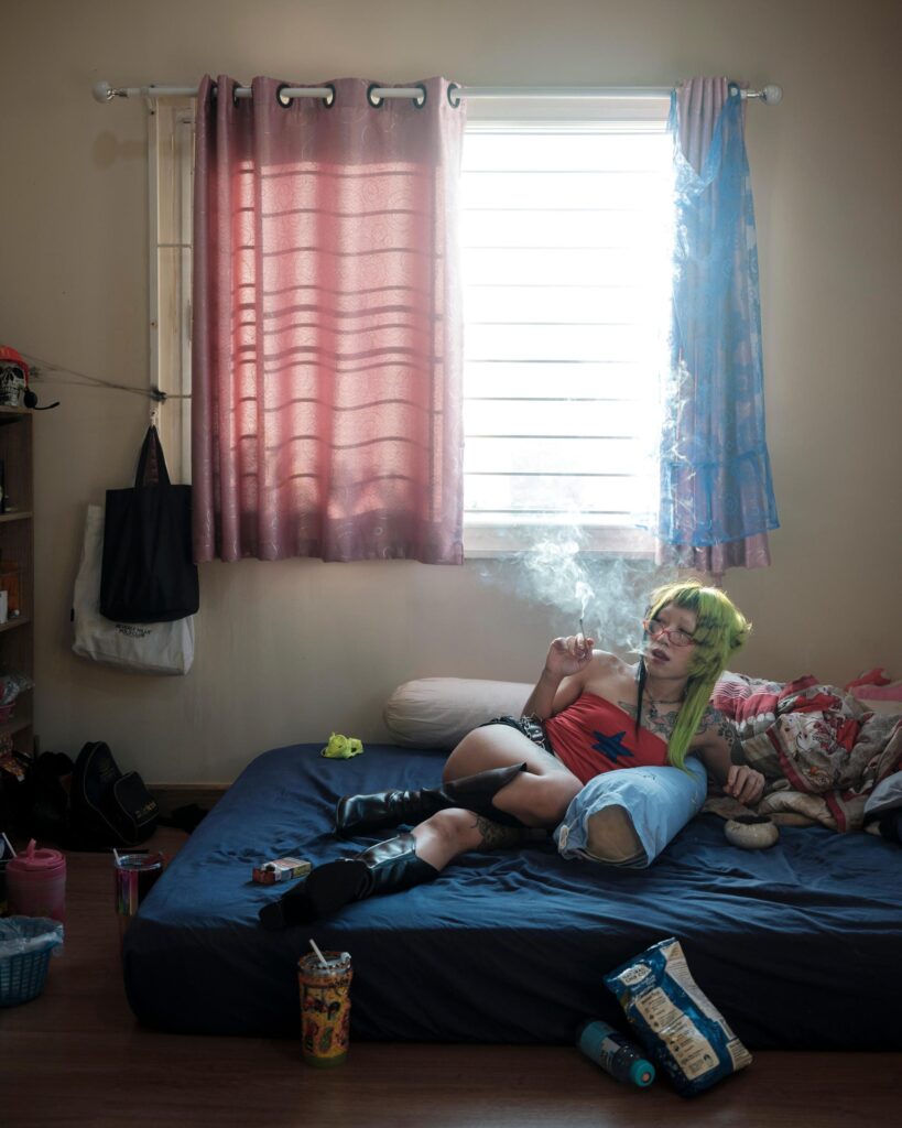 Pemika Wongsurakarn (Sadsadgirl) reclining on a bed beneath a sunlit window in Samut Sakhon.
