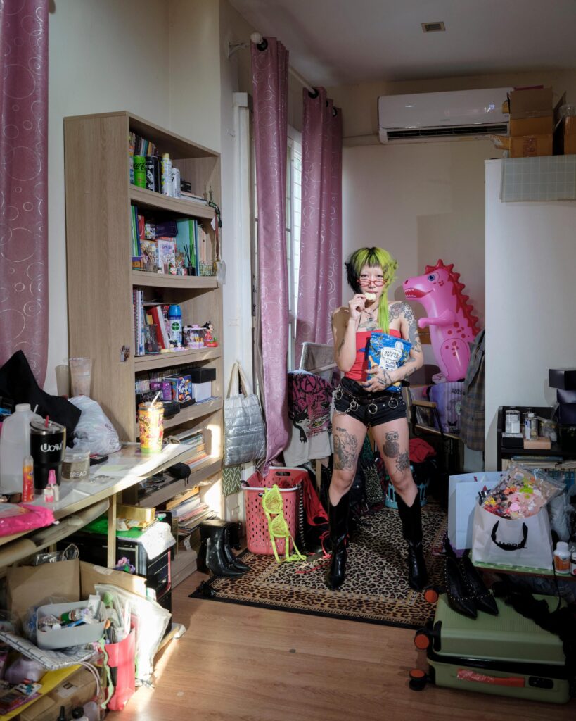 Pemika Wongsurakarn (Sadsadgirl) standing among artworks and objects in her Samut Sakhon room.