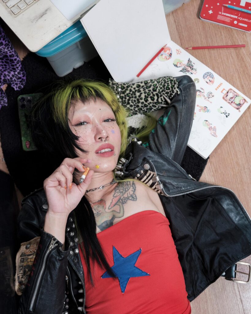 Pemika Wongsurakarn (Sadsadgirl) reclining in a red top and leather jacket, photographed from above in Samut Sakhon.