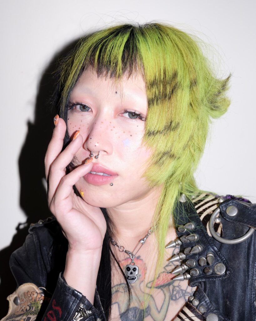 Close portrait of Pemika Wongsurakarn (Sadsadgirl) with green hair and facial piercings in Samut Sakhon.