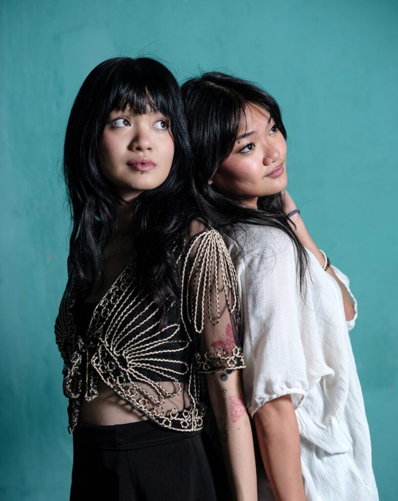 Phoenixe and Klein standing back to back against a turquoise wall in Bangkok.