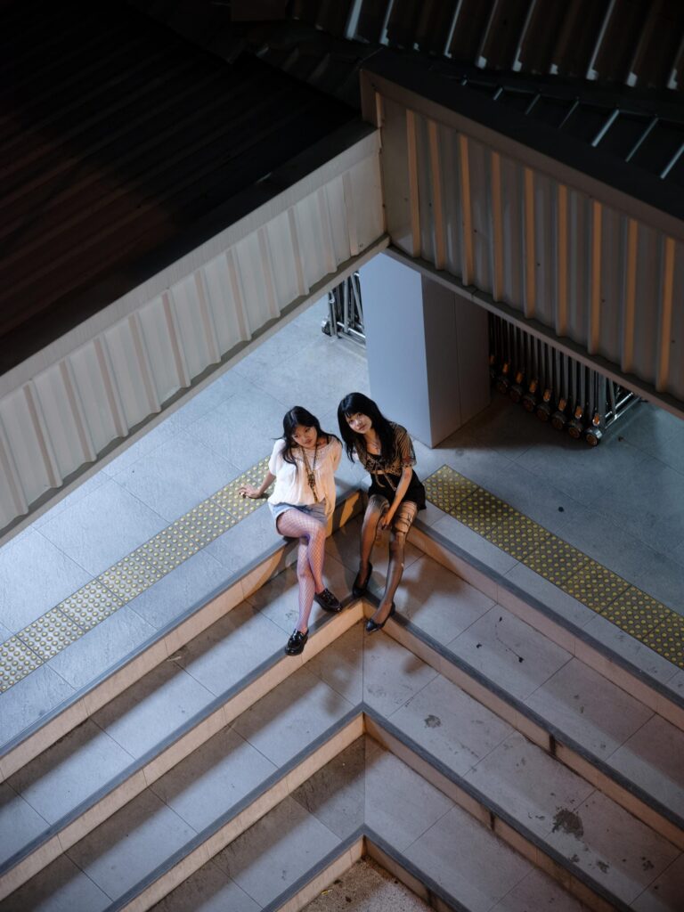 Phoenixe and Klein sitting together on a staircase in Bangkok, photographed from above.