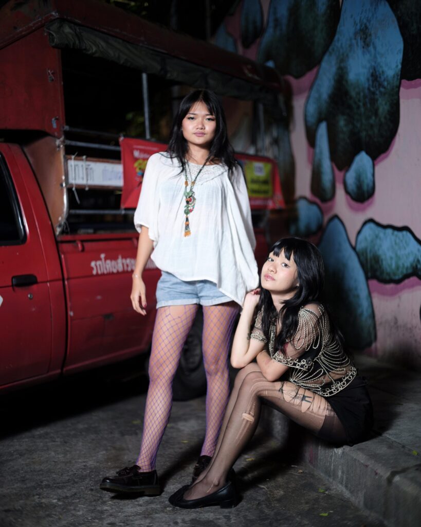 Phoenixe and Klein beside a red pickup truck and painted wall in Bangkok.