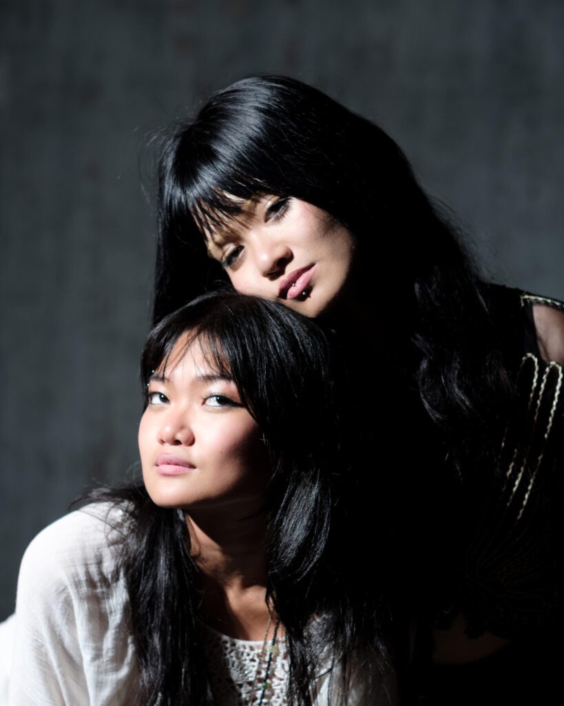 Close portrait of Phoenixe and Klein together against a dark background in Bangkok.