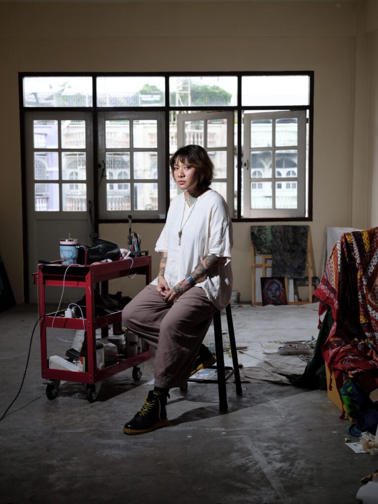 Ploypim seated beside a red trolley and artworks in her Bangkok studio.