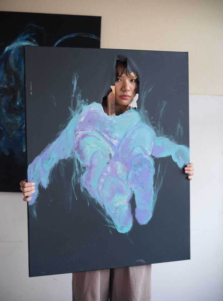 Ploypim holding a painted canvas with her face visible through a cut-out in Bangkok.