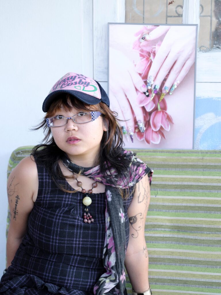 Q3Q Community member wearing a cap and glasses, seated before a nail-art photograph in Bangkok.