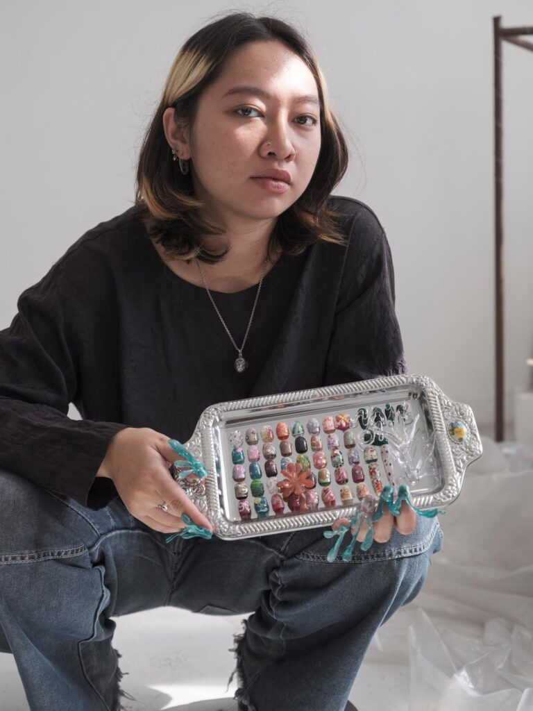 Q3Q Community member in a black shirt holding a tray of nail-art designs in Bangkok.