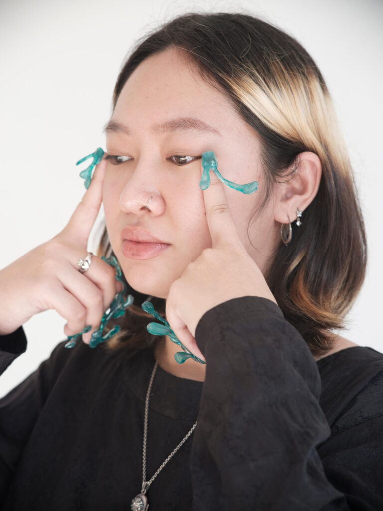 Q3Q Community member framing their eyes with green decorated nails in Bangkok.