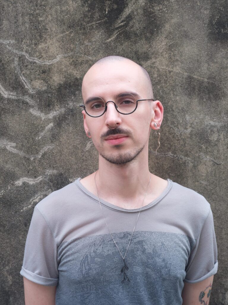 Close portrait of Roman Solodkov (Palindroma) against a textured concrete wall in Bangkok.