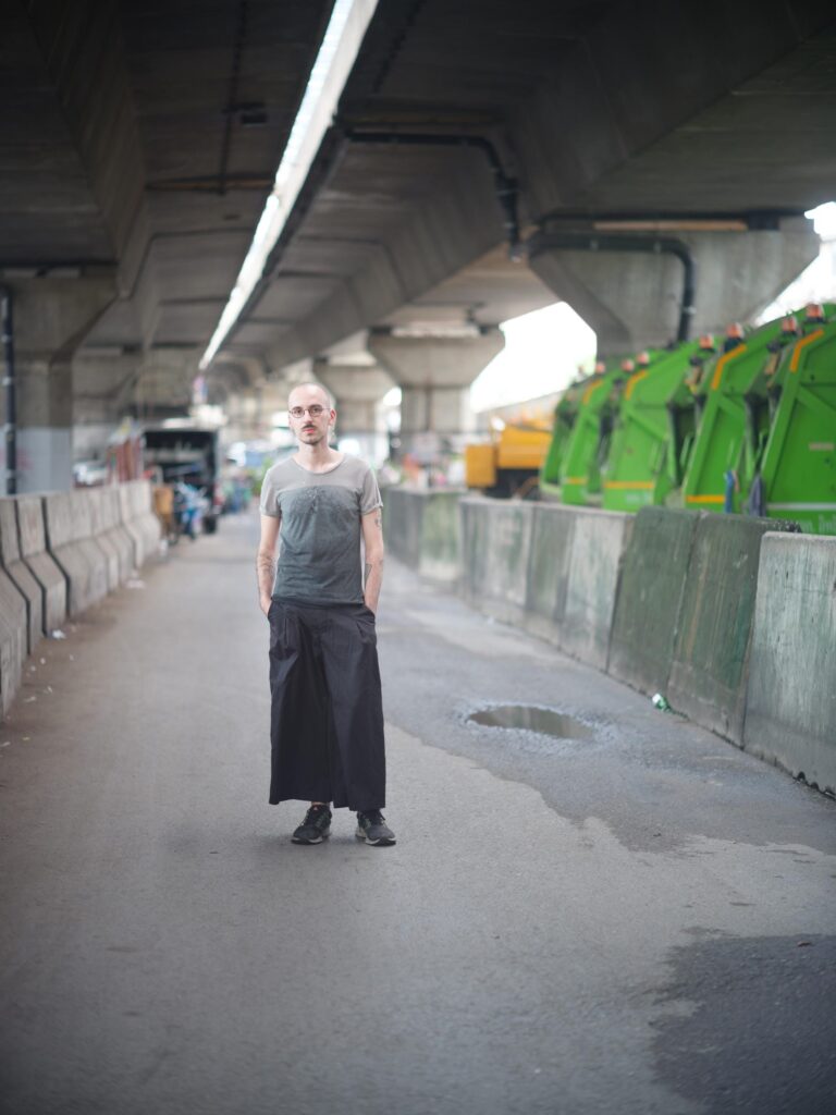 Roman Solodkov (Palindroma) standing on a road beneath a concrete overpass in Bangkok.