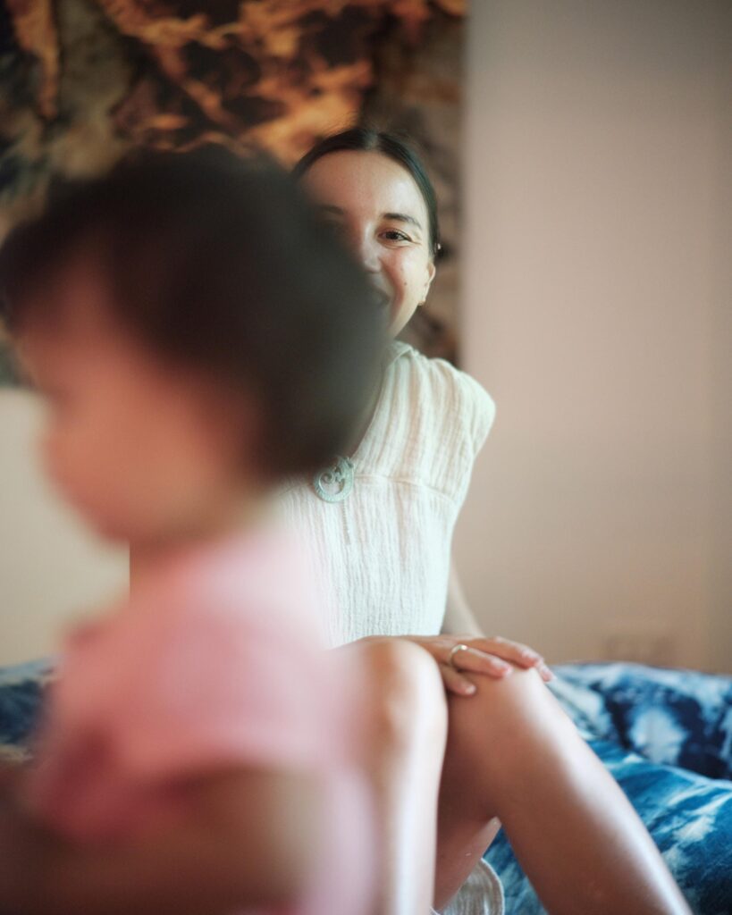 Rosalia Engchuan seated indoors with a child out of focus in the foreground in Bangkok.